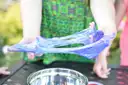 Two hands stretching shiny purple slime above a metal bowl