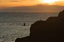 A lone kayaker on open water under an orange sunset