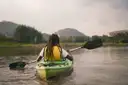 A paddler in a life vest and a green kayak on a calm river
