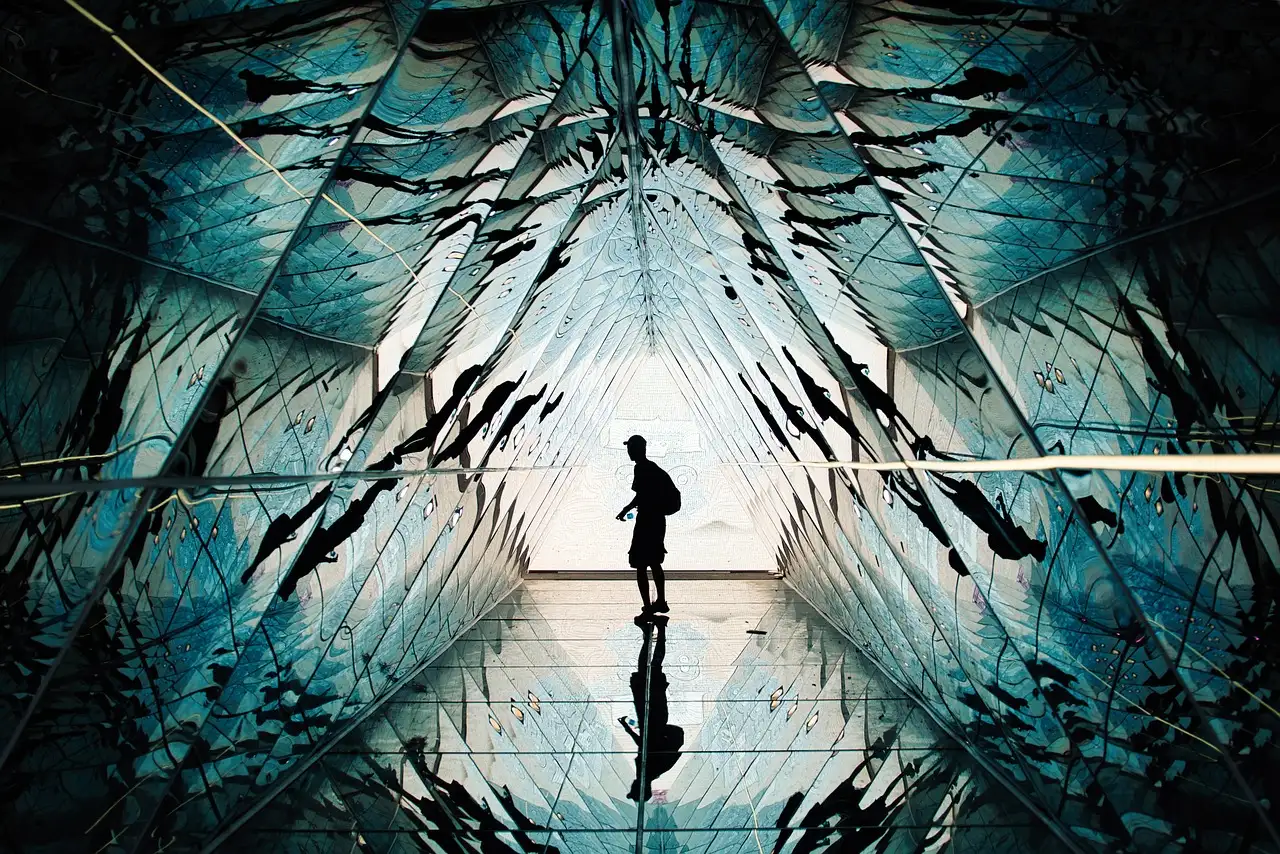 A person in silhouette inside a walk-through installation of angled mirrors