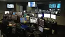 A modern control room with rows of desks and many screens