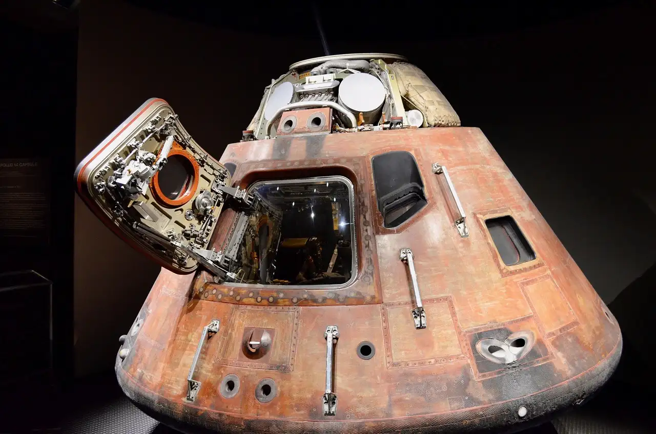 A scorched Apollo command capsule with its hatch open, lit in a dark museum room