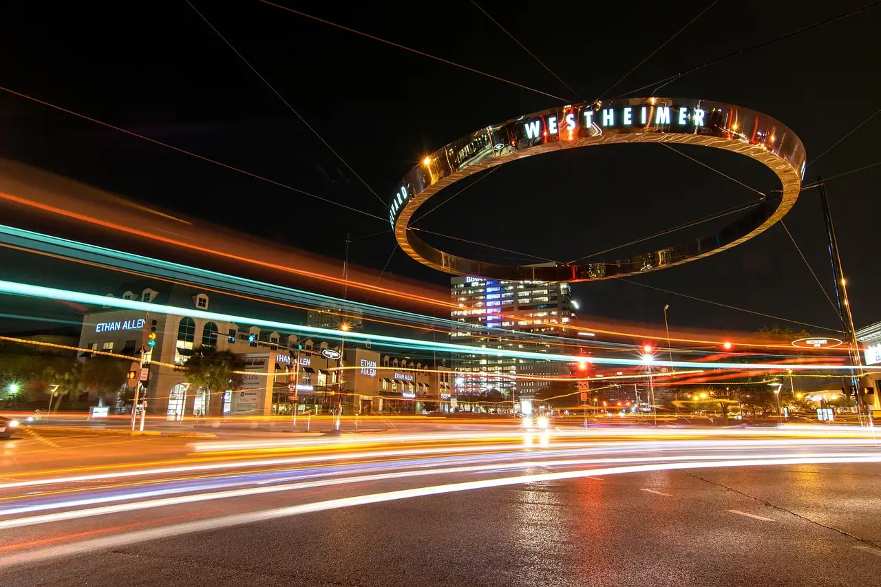 The lit Westheimer ring over Post Oak Boulevard in Uptown Houston at night, with car light trails
