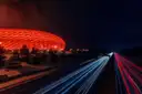 The Allianz Arena glowing red at night beside a motorway with light trails