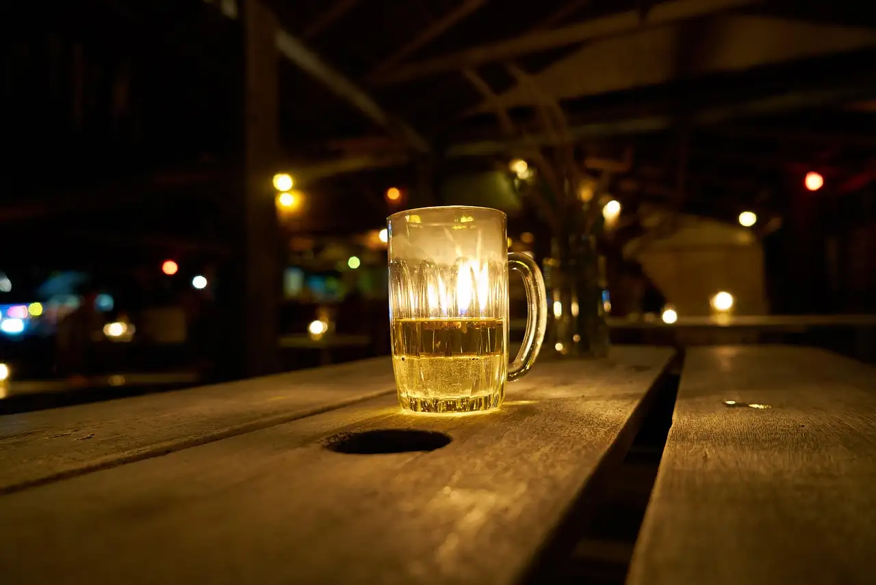 A glass mug of beer on a wooden table in a beer garden at night