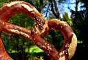 A large salted pretzel held up in front of green trees