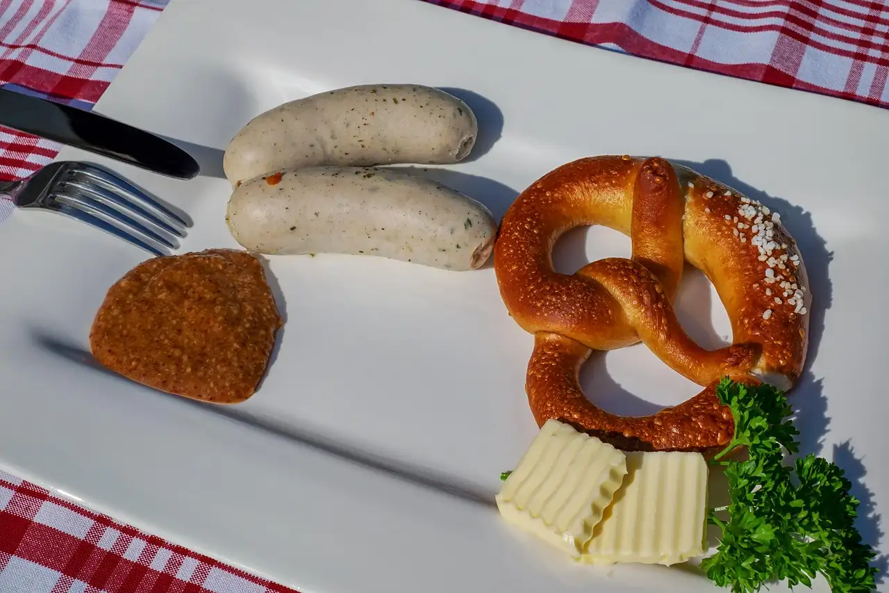 Two white sausages, a pretzel, sweet mustard and butter on a white plate
