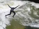 A surfer in a wetsuit riding the standing wave of the Eisbach in Munich