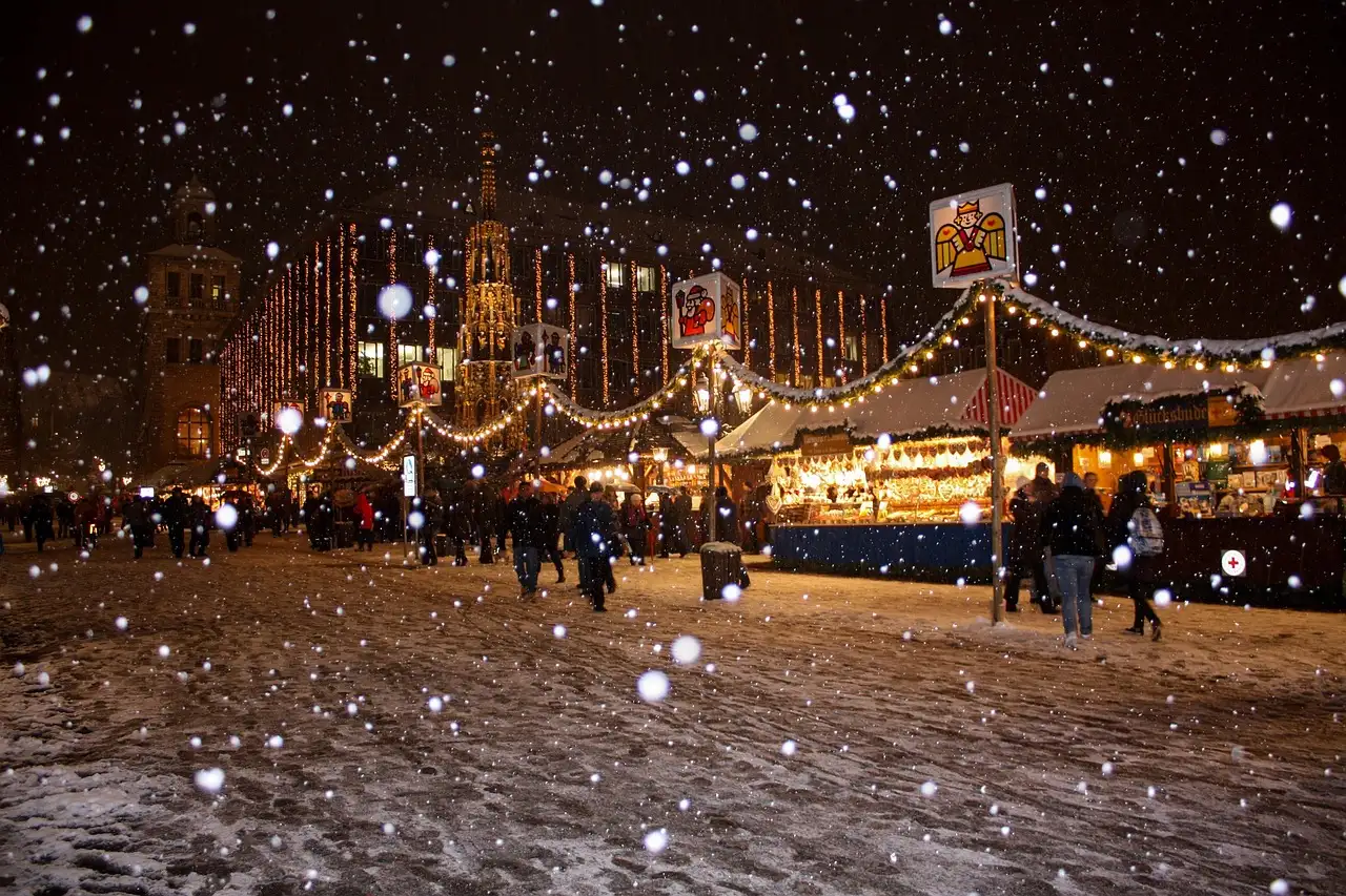 Snow falling on a lit Christmas market square at night