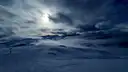 Snow-covered mountain slopes under a dark, cloudy sky