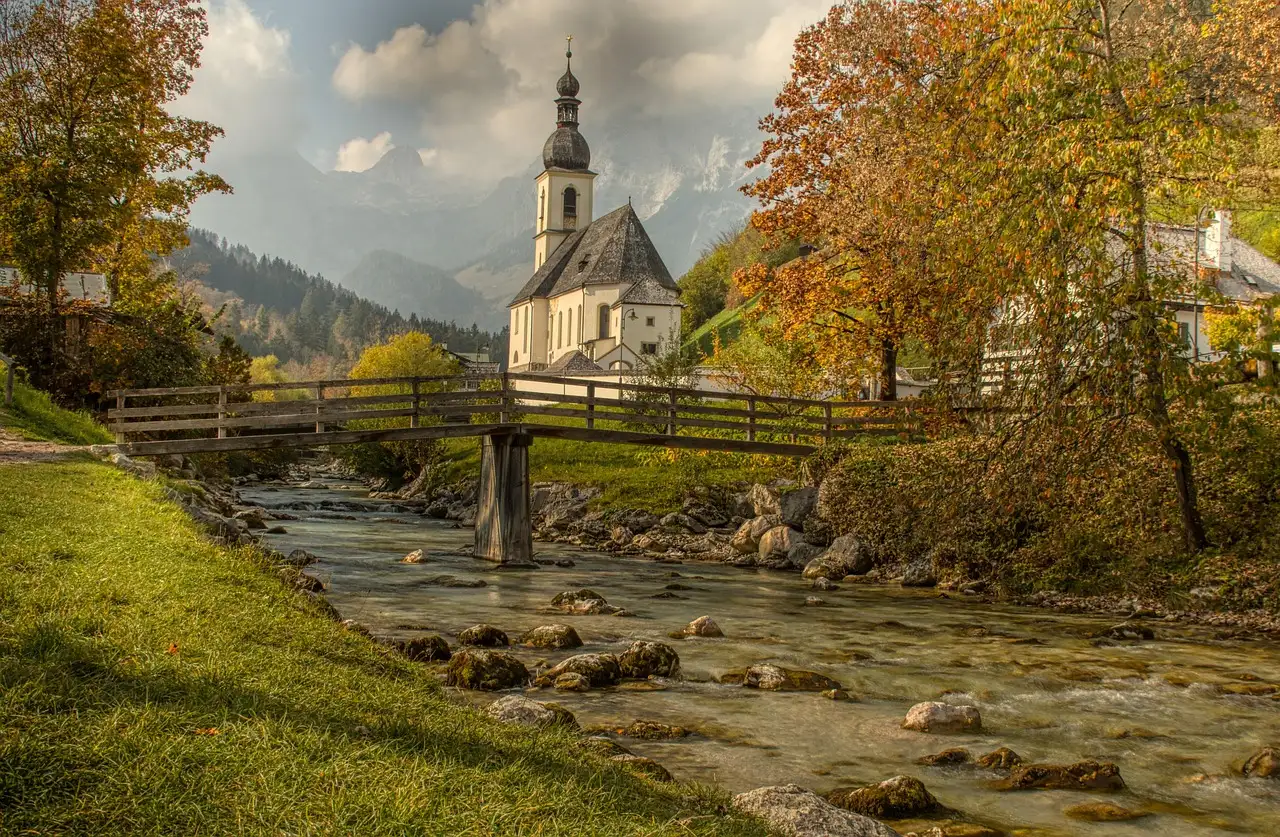 The church of Ramsau above a wooden bridge and a stream in autumn