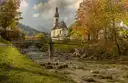 The church of Ramsau above a wooden bridge and a stream in autumn