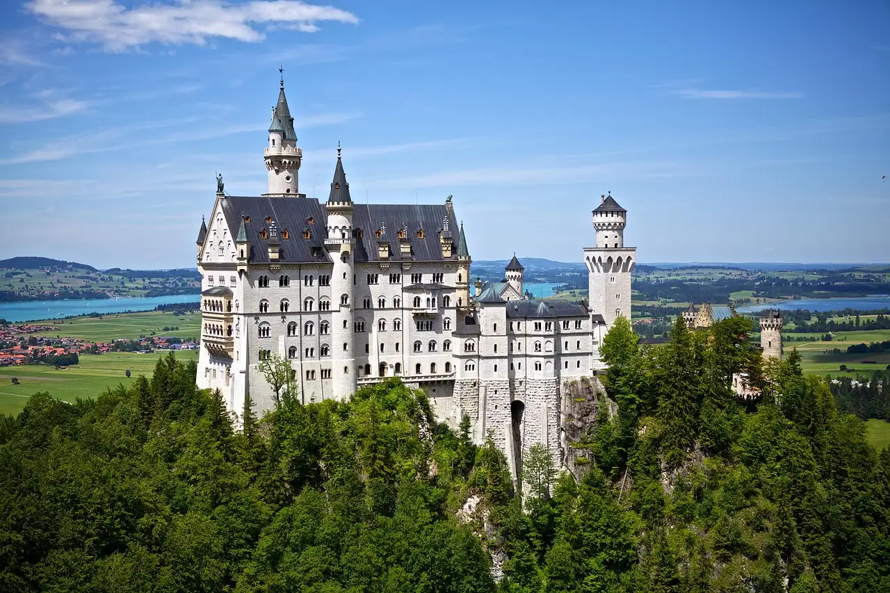 Neuschwanstein Castle above green forest, with lakes in the distance