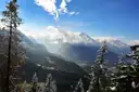 View over the Berchtesgaden valley toward snow-covered Alpine peaks, seen through snowy fir trees