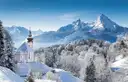A small church on a snowy hill in front of the Bavarian Alps