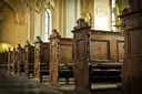 Carved wooden pews in an old chapel, lit by window light