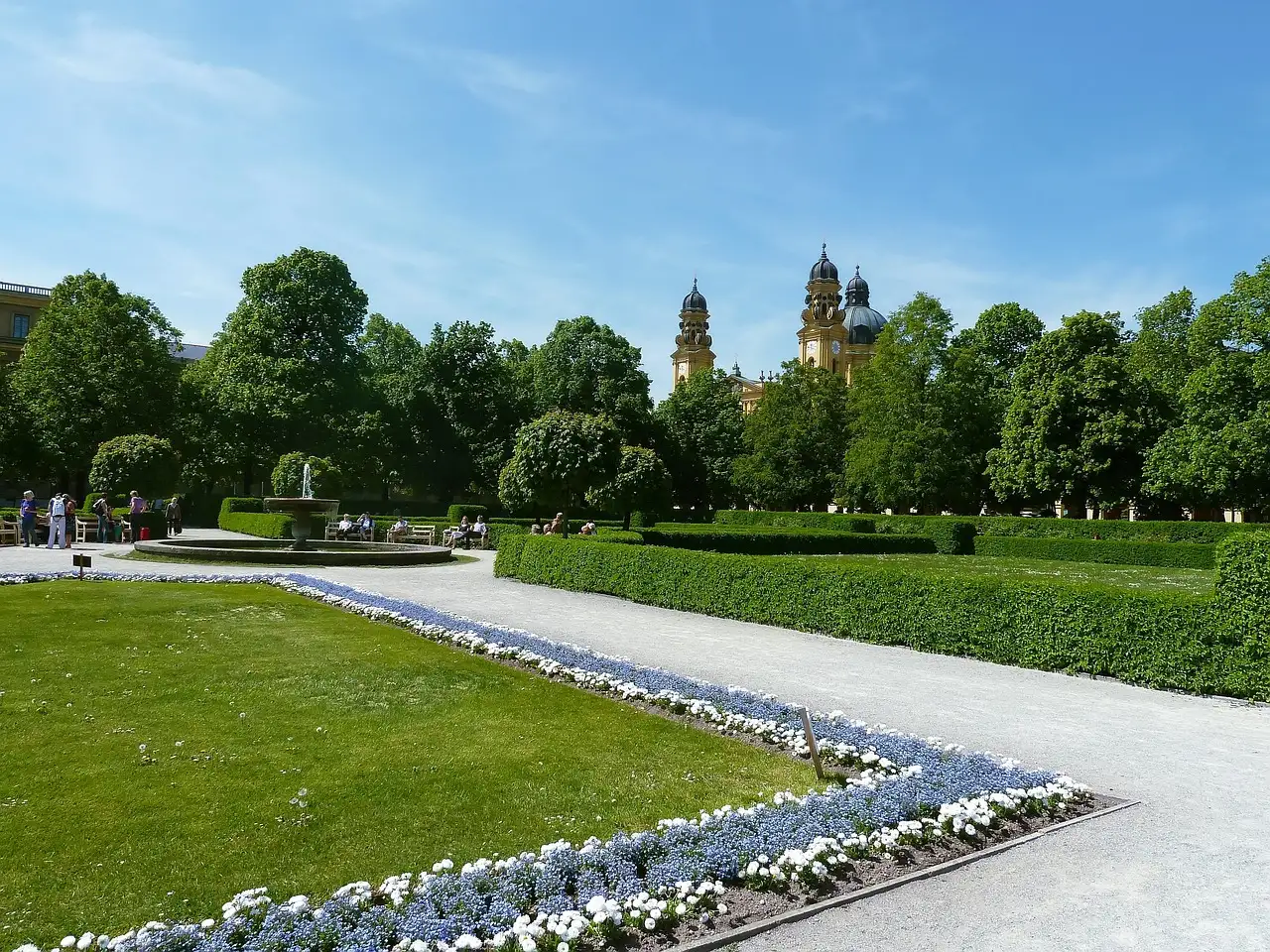 Flower beds and paths in the Court Garden in summer, with church towers behind the trees