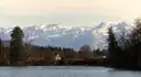 A pond in Salzburg with trees on its shore and snowy mountains behind