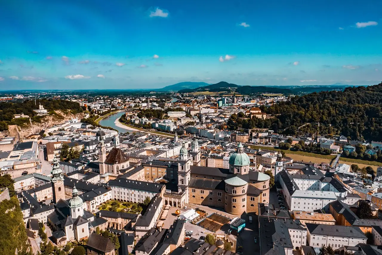 Salzburg's old town roofs and church domes from above, with hills behind