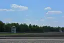The empty roll-call ground at the Dachau memorial with a watchtower and trees under a blue sky