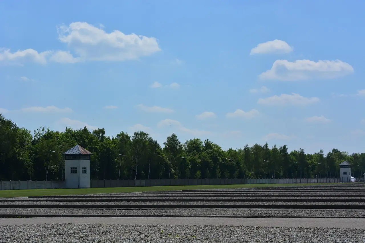 The empty roll-call ground at the Dachau memorial with a watchtower and trees under a blue sky