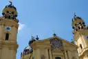 The yellow towers and dome of the Theatine Church in Munich against a blue sky