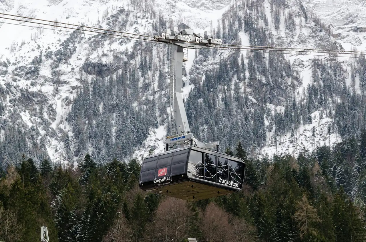 A cable car cabin above a snowy forest, with rocky mountain walls behind