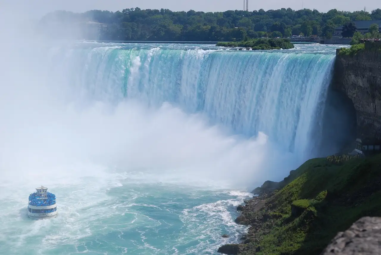The Horseshoe Falls by day, with green water, rising mist and a tour boat below