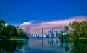The Toronto skyline and CN Tower across calm water, framed by the green, tree-covered shores of the Toronto Islands.