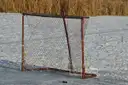 A red hockey net and a black puck on a snowy frozen pond