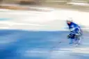 A hockey player in blue skating fast across the ice, blurred by speed