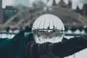 A glass ball in falling snow at Nathan Phillips Square, the skating rink's arches behind