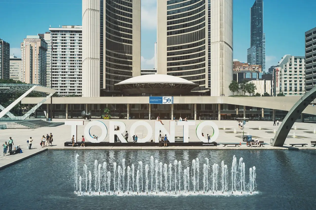 Toronto City Hall and the TORONTO sign on Nathan Phillips Square, fountains in the pool, sunny day