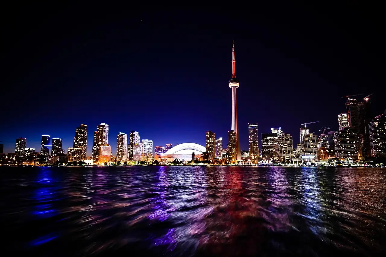 The Toronto skyline and the CN Tower lit up at night, reflected in the lake