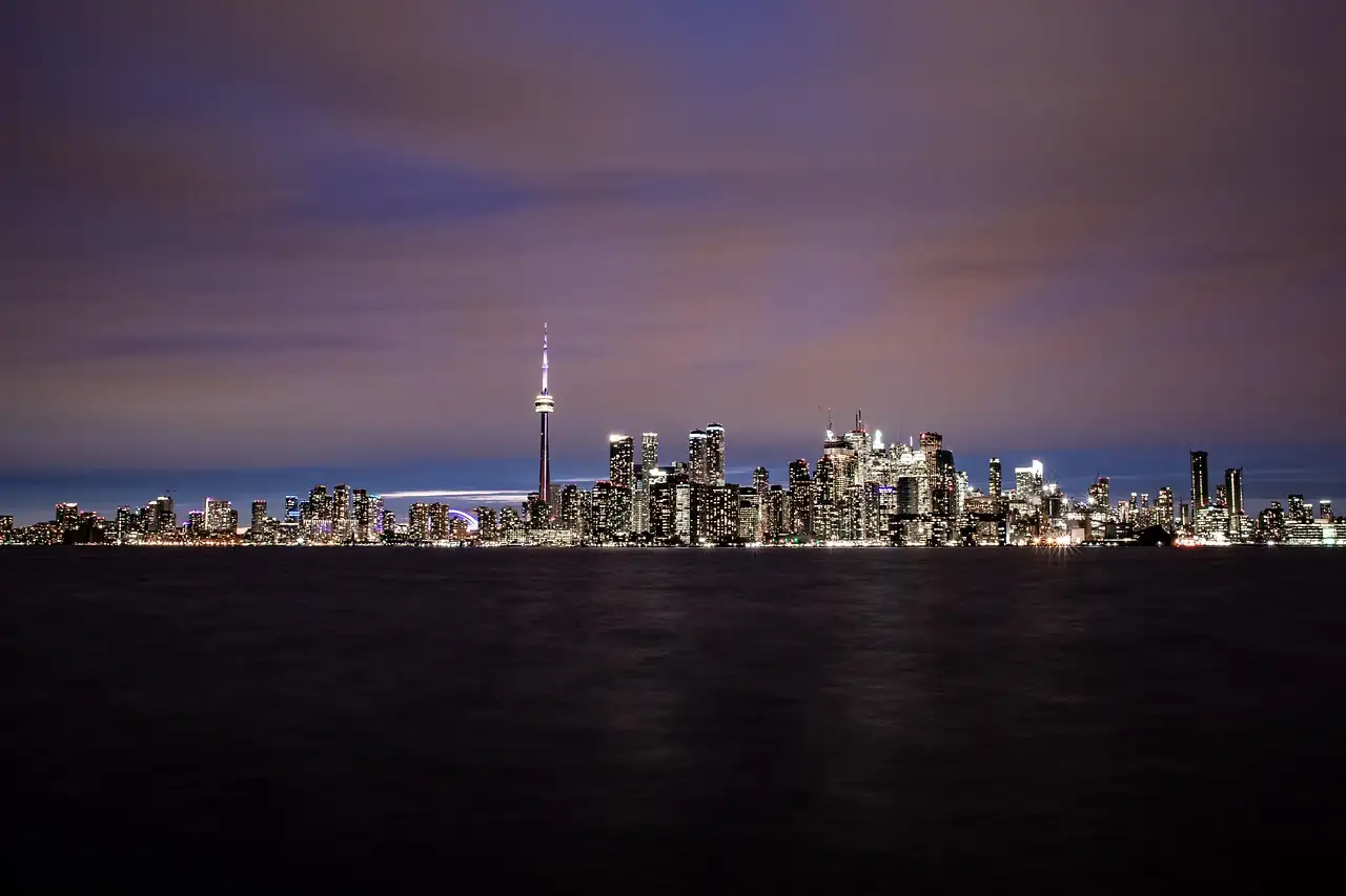 The lit Toronto skyline and CN Tower across dark water at night, under a purple sky.