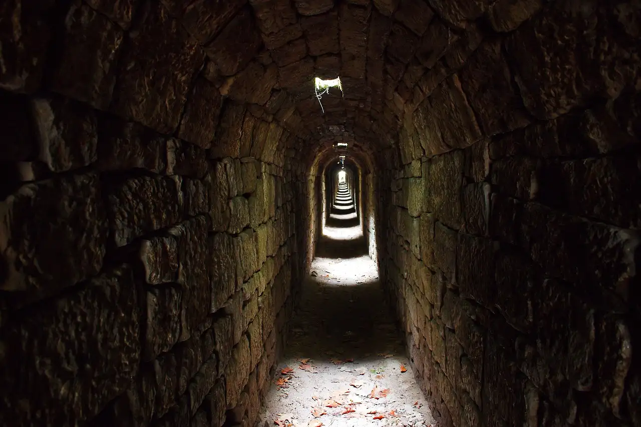 A narrow stone tunnel with light at the far end