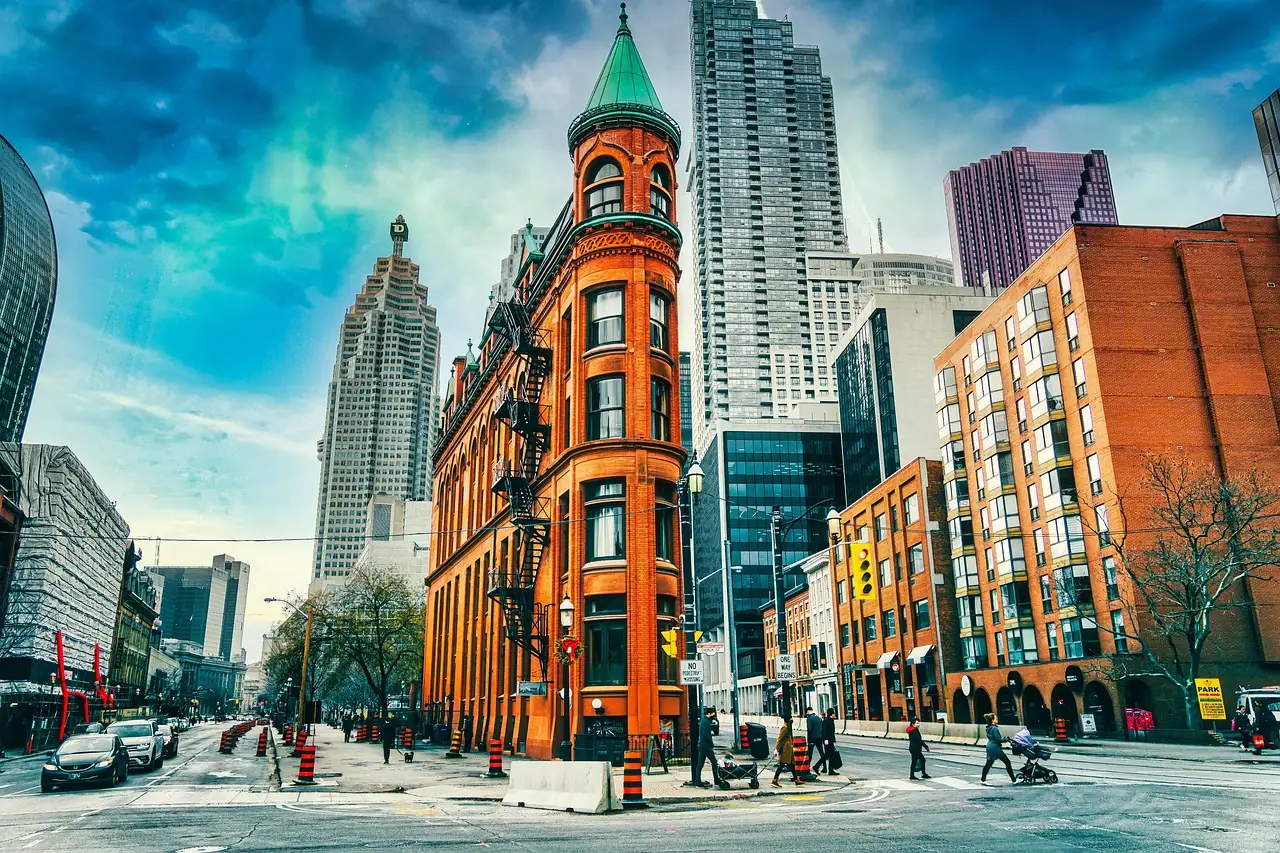 The red-brick Gooderham (Flatiron) Building at a downtown Toronto street corner, with tower blocks and pedestrians beside it.