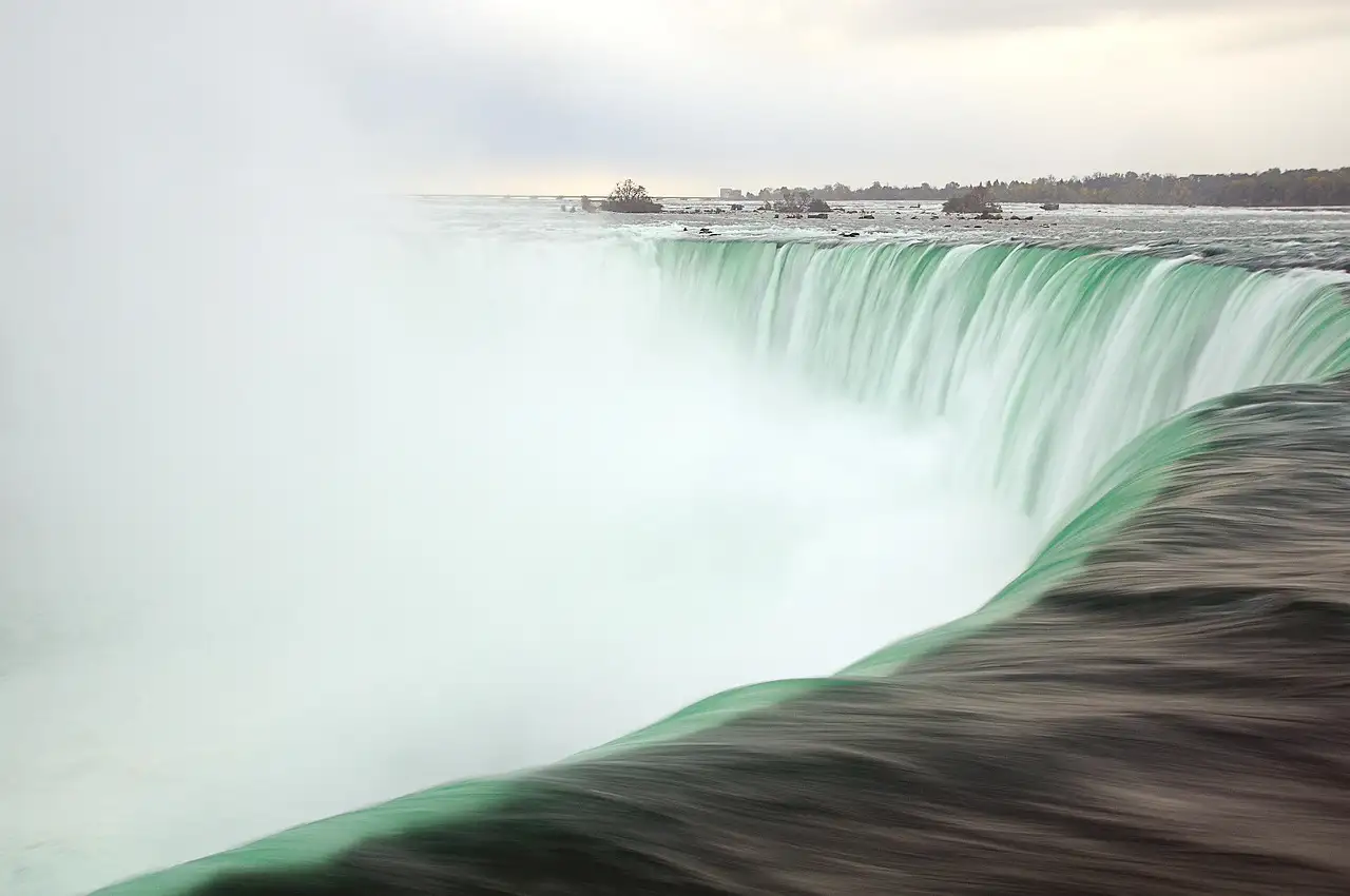 Green water sliding over the edge of the Horseshoe Falls into white mist