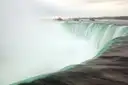 Green water sliding over the edge of the Horseshoe Falls into white mist