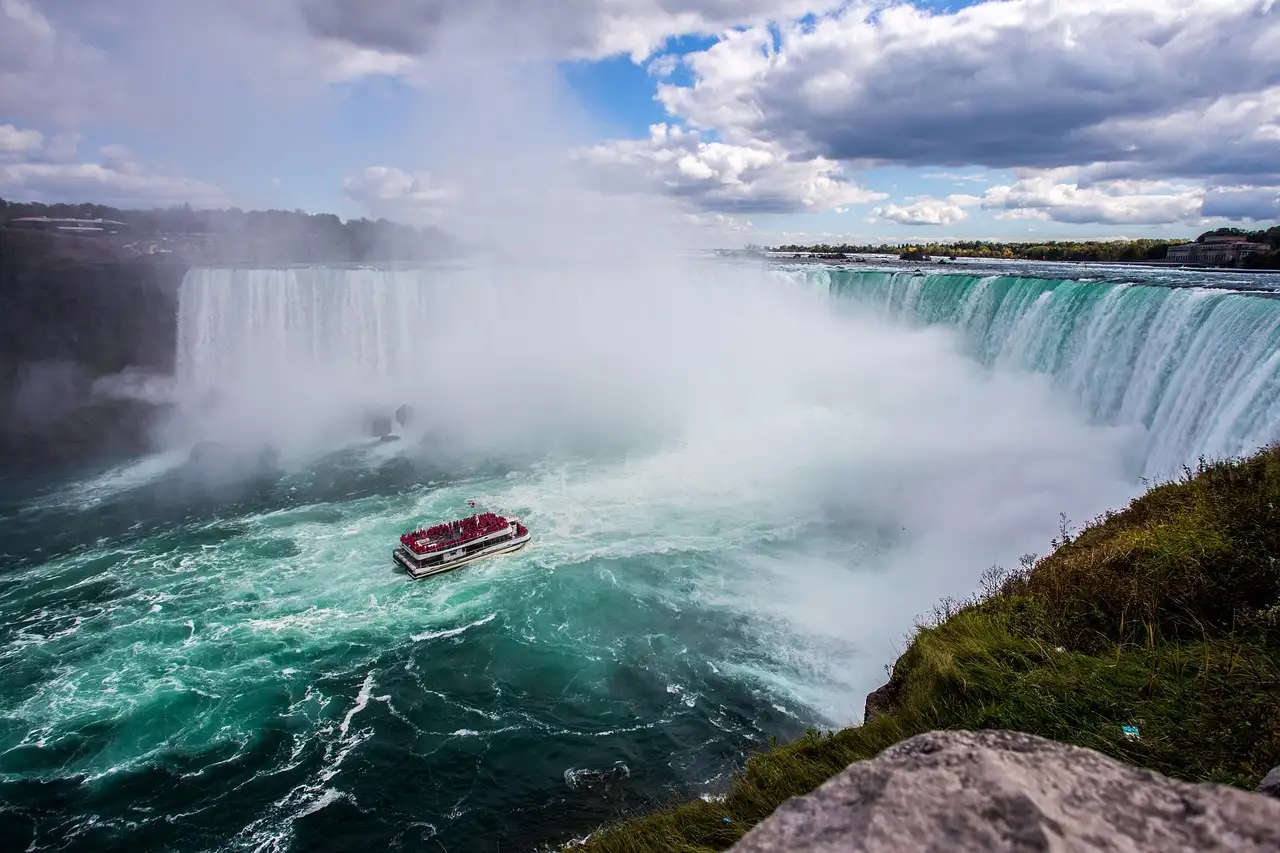 A red boat full of passengers in the churning water below the Horseshoe Falls, seen from the cliff