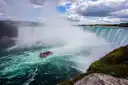 A red boat full of passengers in the churning water below the Horseshoe Falls, seen from the cliff
