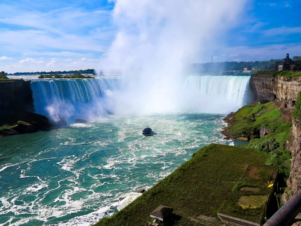 The Horseshoe Falls and its mist seen from the high Canadian bank, with a boat on the river