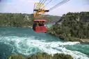 A red cable car hanging over the green river in the Niagara gorge