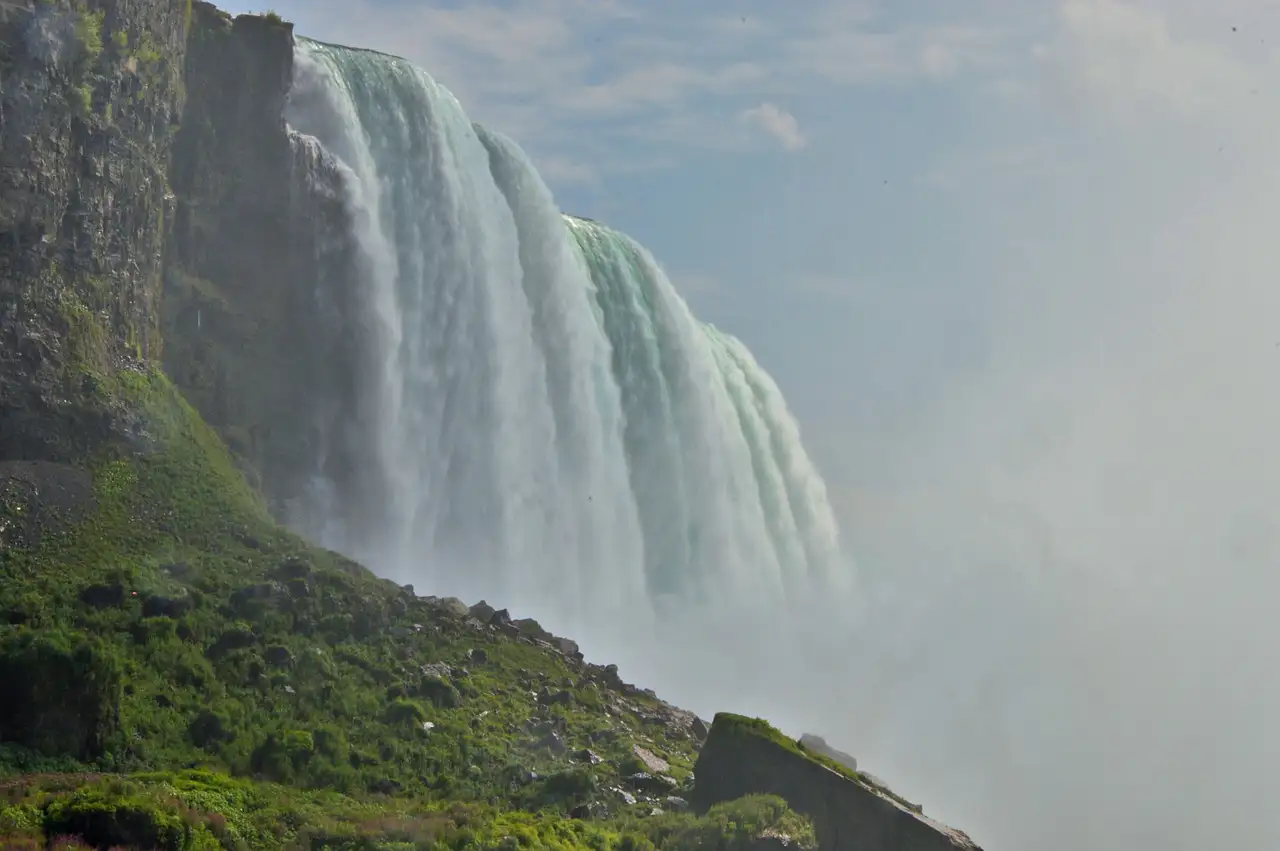 A wall of falling water and spray seen from below, beside a green slope