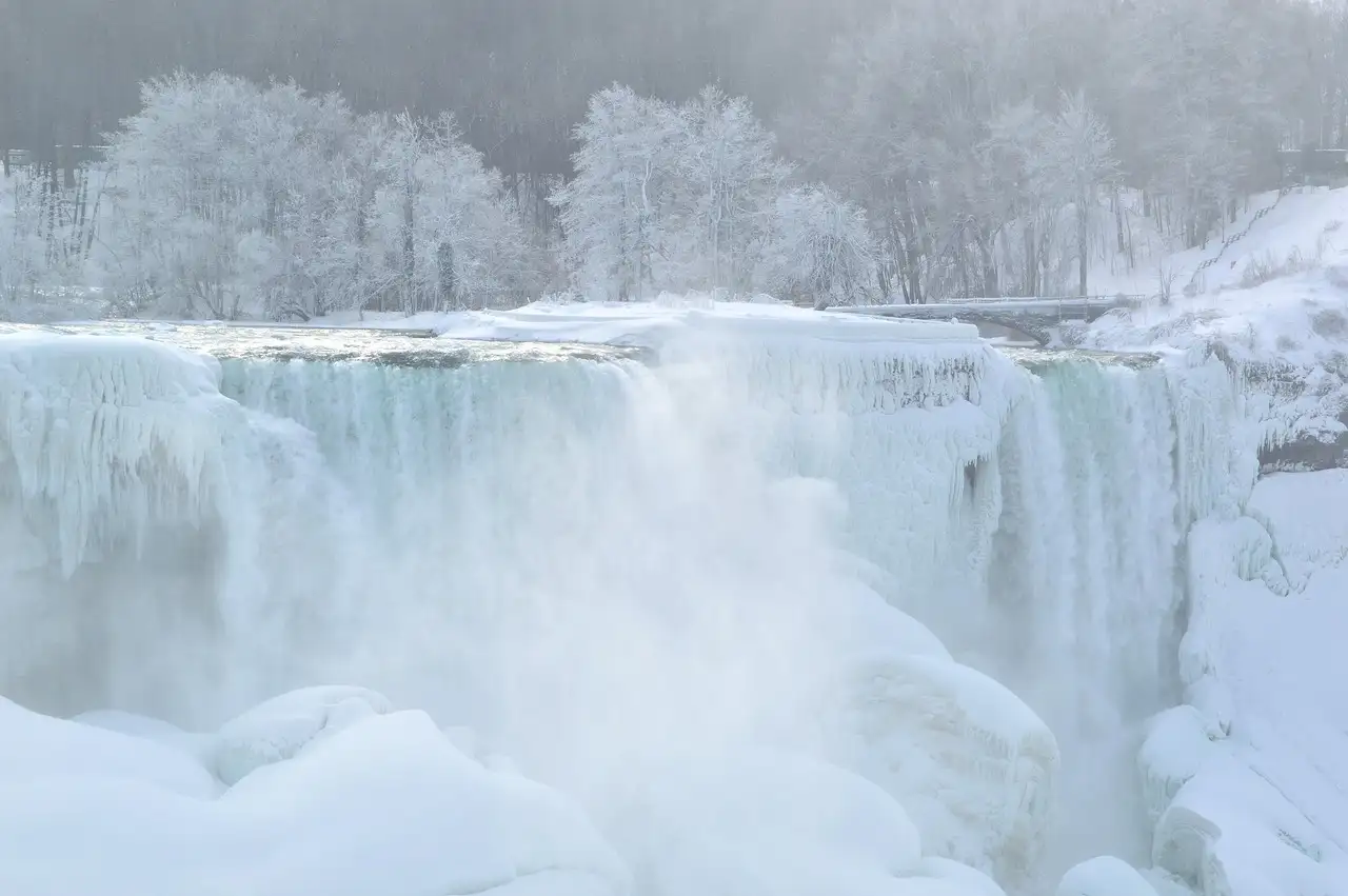 The American Falls half frozen in winter, with frosted trees behind