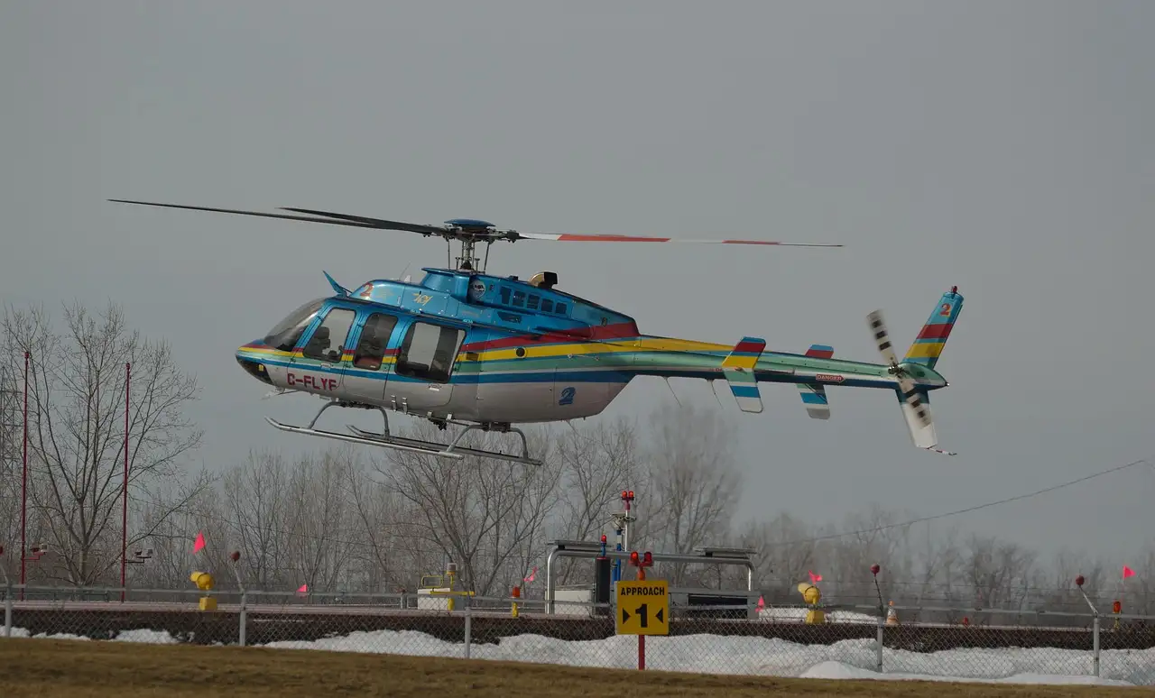 A blue helicopter with rainbow stripes lifting off from a heliport