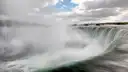 Green water pouring over the curved edge of the Horseshoe Falls into the mist
