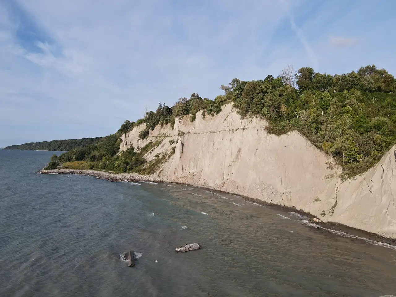 The pale clay Scarborough Bluffs rising above the grey-blue water of Lake Ontario, with green trees along the top.