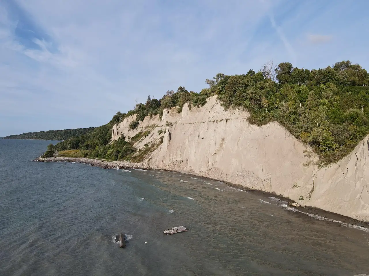 The pale clay Scarborough Bluffs rising above the grey-blue water of Lake Ontario, with green trees along the top.
