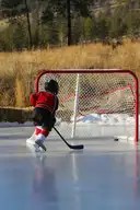 A child in a red hockey jersey skating toward a hockey net on an outdoor rink